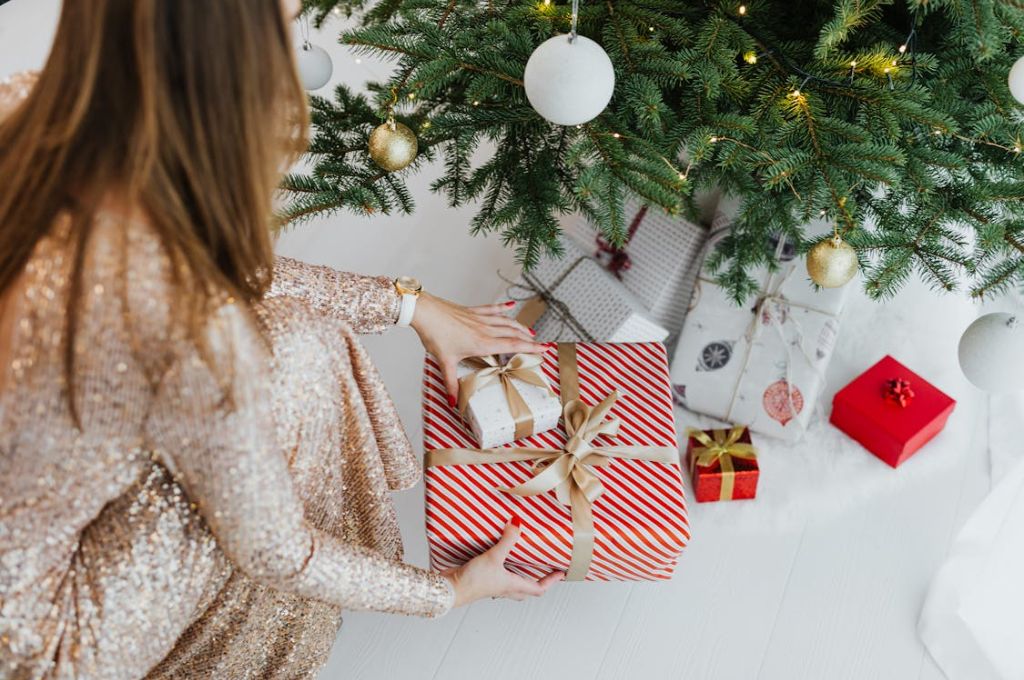 Woman packing gifts under her Christmas tree as a Wholesome Thing to Do Alone on Christmas Day